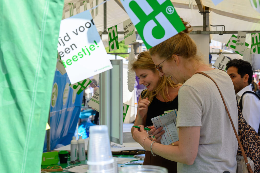 Bezoekers bekijken lachend informatie bij een stand op De Banenmarkt Groningen