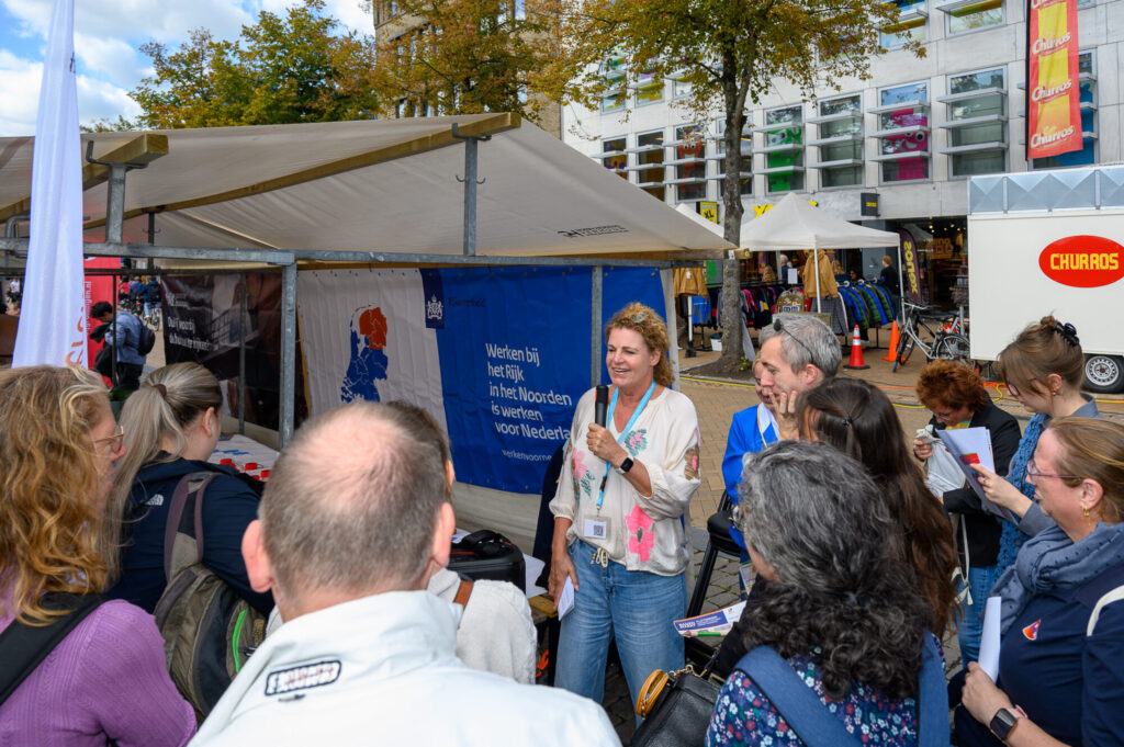 Flight Tour op De Banenmarkt Groningen: een werkgever presenteert haar bedrijf met een microfoon aan een groep werkzoekenden