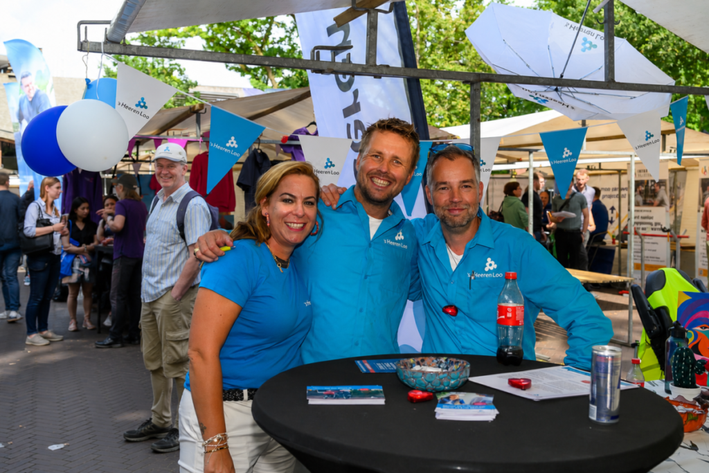 Drie medewerkers van een deelnemende zorgorganisatie bij hun stand op De Banenmarkt